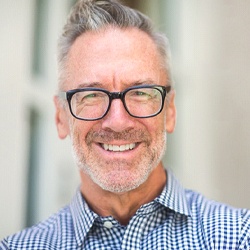 Older man in glasses smiling while wearing a collared shirt