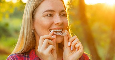 Woman in flannel shirt putting in SureSmile clear aligner in Odessa, TX